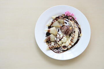 Roti cut into bite-sized pieces with banana and fried. Served with vanilla ice cream, whipped cream, sliced ​​almonds. and sliced ​​banana Topped with chocolate, decorated with pink flowers. Served in