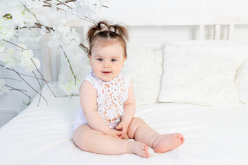 happy baby girl in a white bodysuit on the bed at home in a bright room smiling