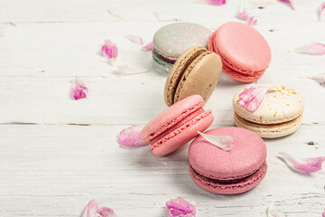 Macarons with peony flower petals on a white wooden background. Sweet dessert, pastel colors