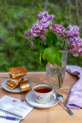 Tea party in the garden with Viennese waffles and a bouquet of lilacs and an open empty notebook for writing on a wooden table on a sunny day. The concept of a new life.