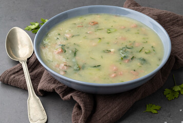 Traditional portuguese green soup with potato, green cabbage and sausage in a bowl over stone background