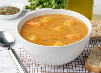 Vegetable soup in a bowl with seasonings and bread slices over wooden table