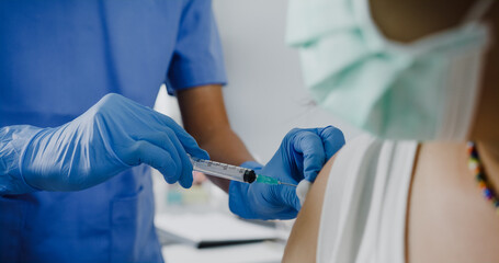 Young Asia lady nurse giving Covid-19 or flu antivirus vaccine shot to teenage girl patient wear face mask protection from virus disease at health clinic or hospital office. Close up or Closeup shot.