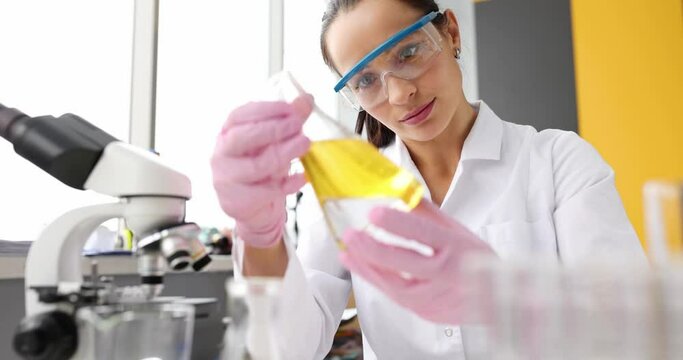 Doctor in protective glasses holds test tube with a yellow liquid in laboratory closeup
