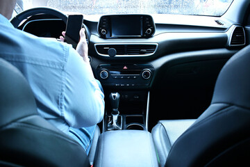 Hombre latino viendo su telefono movil dentro de su auto en el trafico mientras llueve. Hombre de negocios manejando hacia su trabajo. Vista general del interior.
