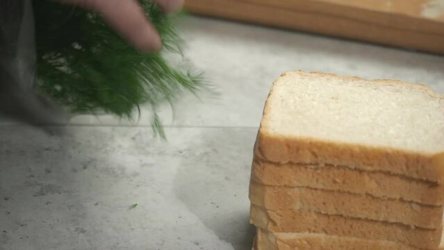 Fresh dill is placed on countertop next to stack of white bread slices