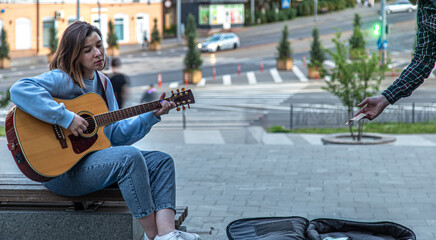 Female musician busking playing acoustic guitar and singing outdoors in street.