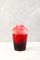 Fruit berries iced cocktail in disposable plastic cup. Slushie - drink. Grey background. Take away food. Refreshing summer drink. Fruit shaved ice with juice
