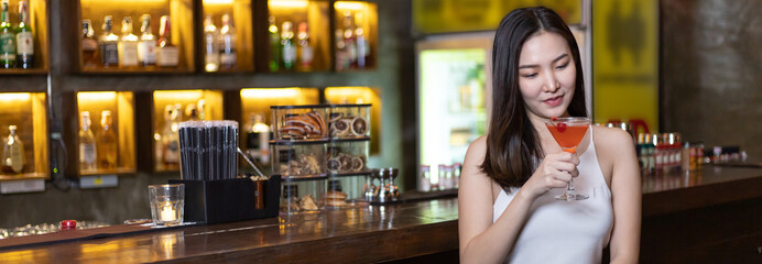 Young Asian woman with a sad face drinking cocktails in front of a vintage bar, Relaxing activities after work or hangouts, Place of entertainment for young adolescents or night club party.