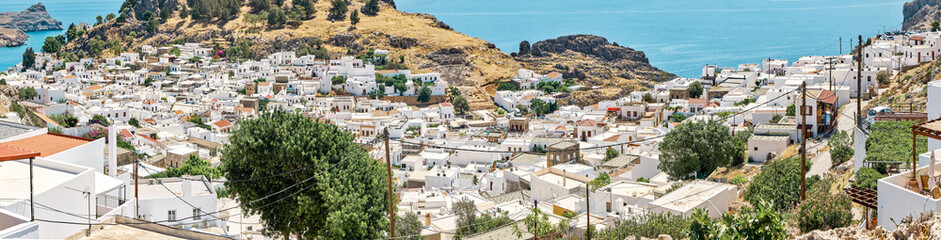 Obraz premium Ancient Lindos city on Rhodes island with white houses and private green gardens scattered on sea bay coast with turquoise water