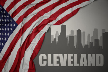 abstract silhouette of the city with text cleveland near waving colorful national flag of united states of america on a gray background.