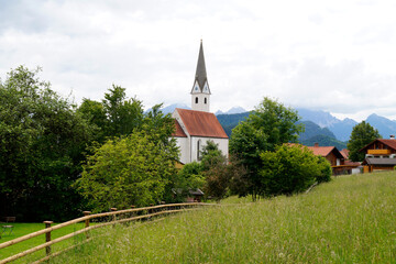 a scenic view with lush green alpine meadows and a beautiful old church in the Bavarian village Schwangau in the Bavarian Alps on a hot summer day (Allgaeu, Bavaria, Germany)	