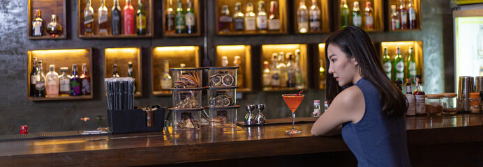 Young Asian woman with a sad face drinking cocktails in front of a vintage bar, Relaxing activities after work or hangouts, Place of entertainment for young adolescents or night club party.