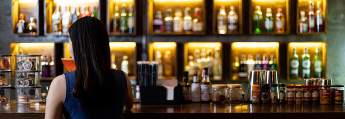 Young Asian woman with a sad face drinking cocktails in front of a vintage bar, Relaxing activities after work or hangouts, Place of entertainment for young adolescents or night club party.