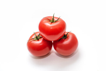 Three juicy tomatoes lie on a white isolated background. Red tomatoes with green stems, top view. Vitamin-rich vegetables in the form of fresh juicy tomatoes in the center of the horizontal image