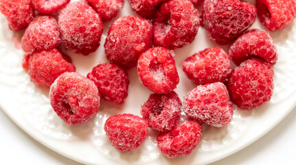 Frozen raspberry on white plate close up. Top view.