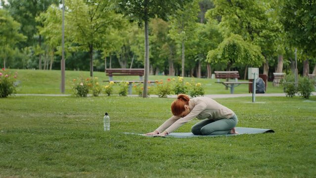 Woman stretching back, yoga poses in the park. Stretching techniques after fitness training on yoga mat. Park sport activities. Healthy lifestyle.