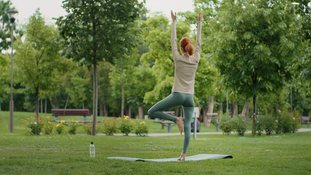 Yoga woman practices yoga and meditates, back view. Healthy female girl sits in pose meditating or practicing yoga in nature outdoors, relaxing. Sport and healthy concept.