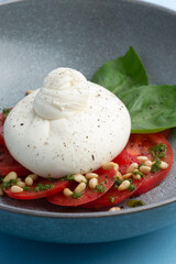 Buratta cheese and tomatoes in a bowl. Decorated with pine nuts.