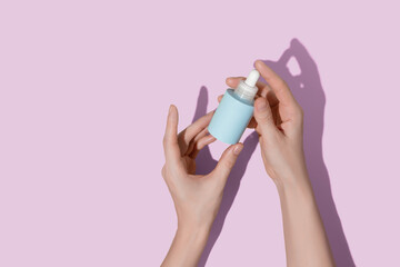 Woman's hands holding blue bottle of cosmetic serum on pink background