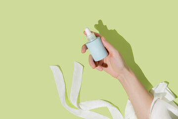 Woman's hand holding blue bottle of cosmetic serum on bright green background. Mockup.