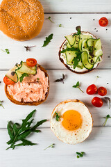 Assortment of sandwiches, white bread, fried egg, cream cheese and cucumber, capelin caviar, sesame bun, breakfast, on a white table, vertical, no people,
