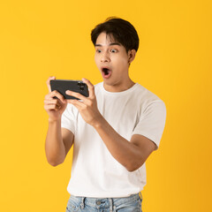 Young good looking asian man using smartphone isolated on yellow background with surprise