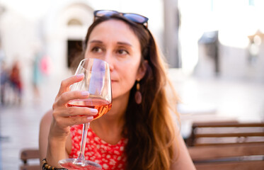 A young girl is relaxing in a summer cafe and drinks rose wine. Selective focus.