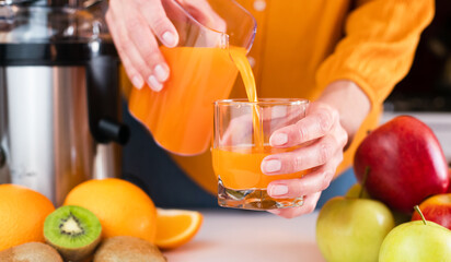 Woman's hands pour freshly prepared tasty and healthy juice into a glass. Healthy fruit juices at...