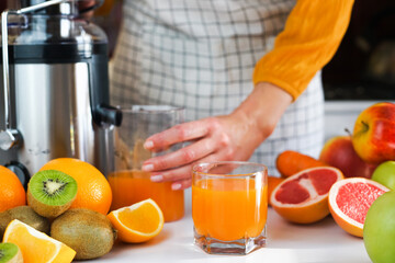 A young woman prepares healthy juice from a variety of ripe fruits in the kitchen at home....