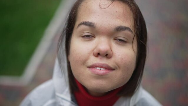 Close-up face of young little woman looking up smiling standing outdoors. Headshot portrait of confident happy Caucasian little person enjoying rainy day in park