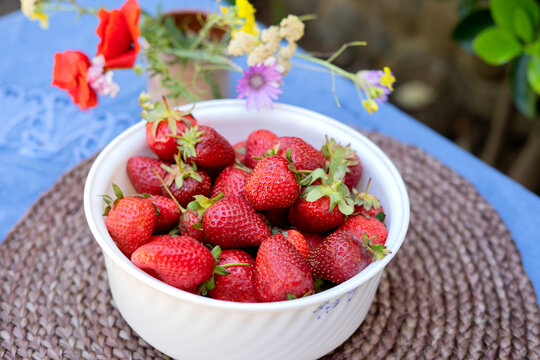 Ripe red strawberries in a white bowl on a table in the garden. Picked strawberries close up.