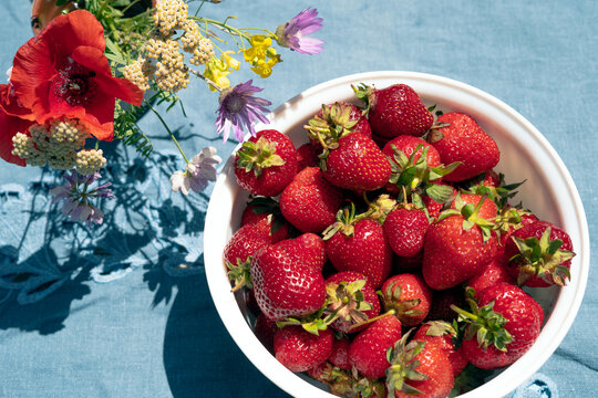 Ripe red strawberries in a white bowl on a table in the garden. Picked strawberries close up.