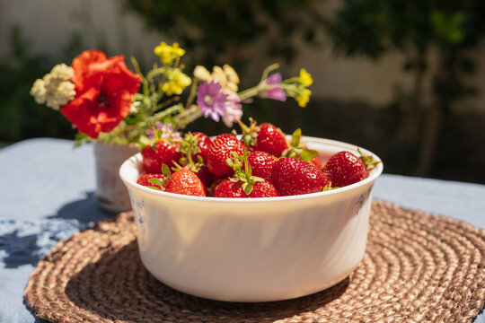 Ripe red strawberries in a white bowl on a table in the garden. Picked strawberries close up.