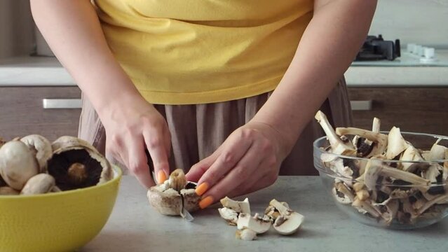 Woman cuts mushrooms with a knife with her hands for soup or sauce. Young woman with a beautiful manicure slices champignons in the kitchen. Close up HD. Brown and yellow colors. Cooks lunch or dinner