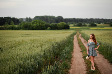 Vinnytsia, Ukraine. May 25, 2022. A girl in a green dress stands in a wheat field and looks at the sky