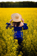 Vinnytsia, Ukraine. May 15, 2022. Ukrainian girl in a hat and blue dress on a background of yellow rape