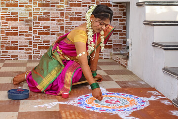 hindu woman in traditional attair drawing rangoli outside home.