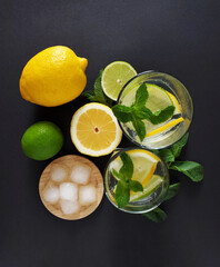 Lemonade in glass glasses with lemon lime sprigs of mint and ice cubes on a dark background 