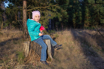 Naklejka na ściany i meble happy five-year-old girl sitting in a jacket on a stump in the woods in the spring