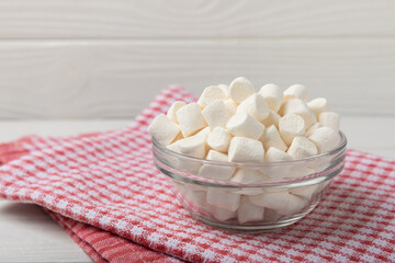 Fototapeta na wymiar Marshmallow in a glass bowl on a white textured background with a rustic napkin.Closeup gummies.Snacks and snacks for parties.Spice for coffee and cocoa.Winter food concept.Place for text.