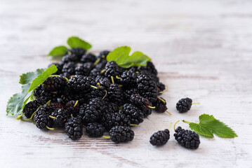 Pile of fresh ripe mulberries with green leaves on the light wooden background. Copy space. Top view