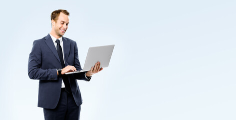 Happy smiling young business man in black suit, necktie using laptop computer, isolated on grey...