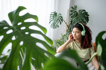 Young woman listening music with headphones on the sofa. She is closed her eyes and thinking about her life with sad expression