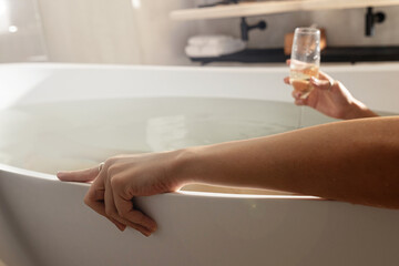Cropped view of the relaxed young woman laying at the bath with hot water and enjoying of glass of champagne. Good moments concept