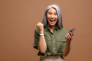 Astonished senior woman holding and using smartphone, mature modern grey-haired lady looking at the...