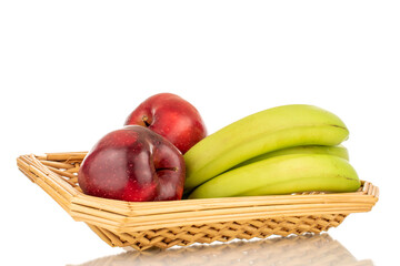 Three sweet yellow bananas and two red apples in a straw bowl, close-up, isolated on a white background.