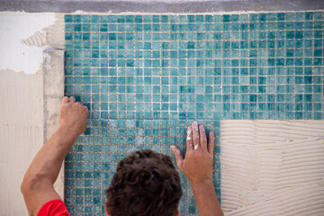 Worker repairing the pool, laying turquoise-coloured gresite tiles - pool repairs