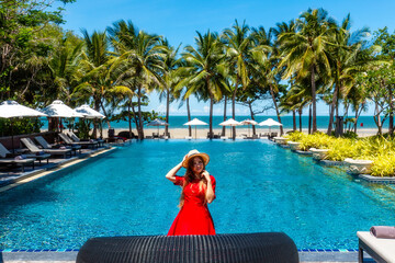 Travel vacation woman in red dress enjoying a summer vacation near swimming pool in tropical resort...