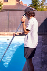 Side view of a young student cleaning a pool during his summer vacation.